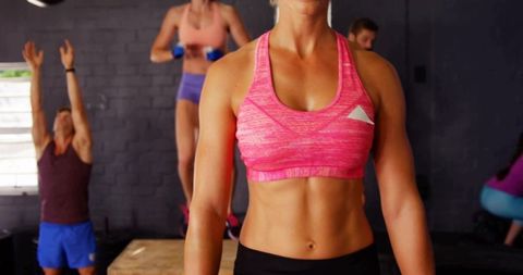 Fit woman showing toned abs in pink sports bra during functional hiit gym class workout