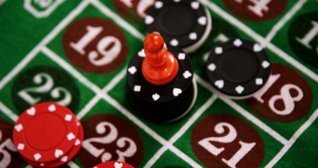 Poker chips and a black peg are scattered over a roulette table, centered on number 19. This image is perfect for themes related to gambling, casino games, betting, risk-taking, and the thrill of chance. It can be used in advertising for casinos, gaming websites, or related industries looking to convey excitement and strategy.