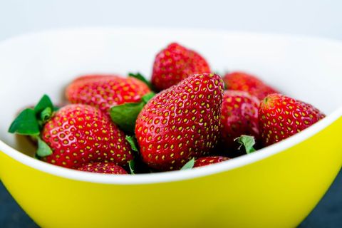 Glossy strawberries resting in yellow bowl close-up, ripe red berries
