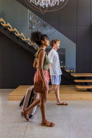 Young couple walking through modern hotel lobby pulling suitcase under chandelier