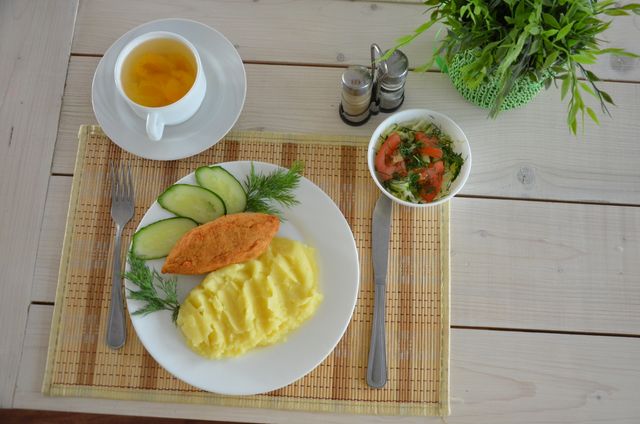 Healthy breakfast showing a cup of tea, mashed potatoes, croquette, and a salad with fresh vegetables, placed on a rustic wooden table with dill garnish. This image is ideal for promoting balanced diets, health food blogs, restaurant menus, nutritional guides, or lifestyle articles focusing on healthy eating and meal planning.