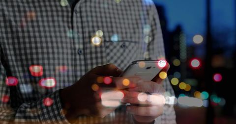 Man Using Smartphone Contrasted with City Bokeh Lights