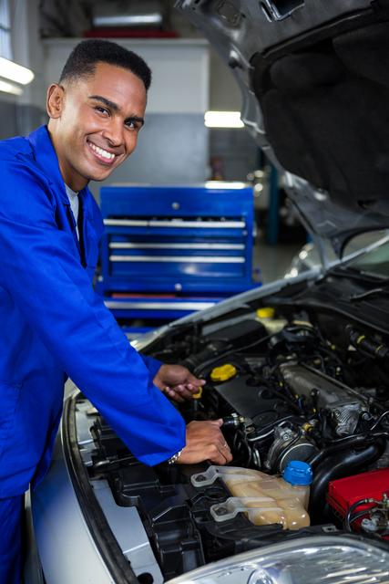 Portrait of happy mechanic checking the oil level in a car engine at repair garage