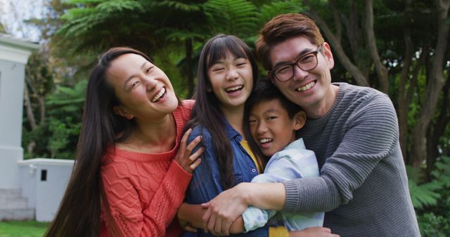 Portrait of smiling asian parents embracing laughing son and daughter in garden. happy family, at home in isolation during quarantine lockdown.