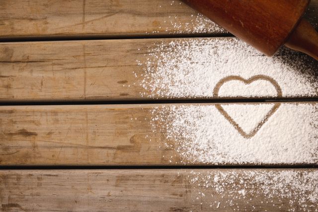 Composition of rolling pin and heart in flour over wooden background. Food autumn and celebration concept.