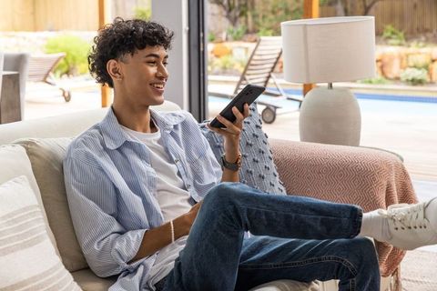 Young man relaxing with smartphone in modern home by poolside