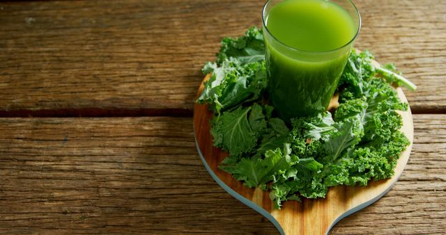 A glass of green juice is surrounded by fresh kale leaves on a wooden cutting board, with copy space. This setup suggests a focus on healthy living and the benefits of including green vegetables in one's diet.
