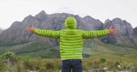 Man embracing mountain view wearing green jacket with outstretched arms