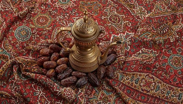 Ornate brass dallah gleaming on red persian textile with cluster of dates flatlay for ramadan