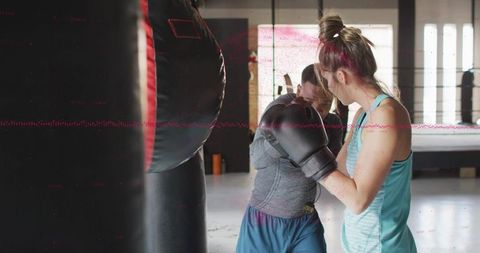 Women sparring close punches by heavy bag in bright boxing gym training