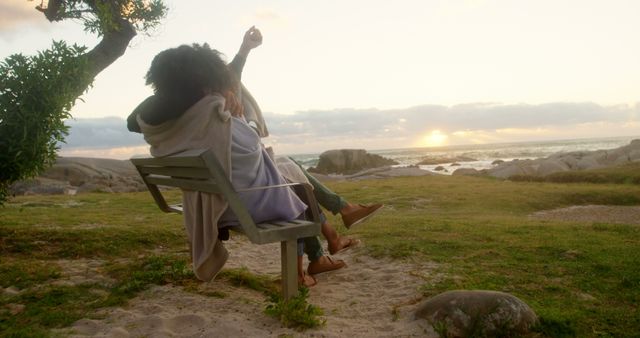 Two people sit on a bench by a tree, facing the ocean, watching the sunset. The scene inspires romance and relaxation, suitable for themes of love, outdoor leisure, and serene getaways. Ideal for travel ads, romance promotions, lifestyle blogs, and nature illustrations.