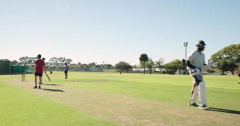 Amateur cricket team practicing on sunny suburban ground with batter walking off pitch