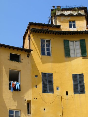 Sunlit Tuscan Yellow Facade with Weathered Shutters, Curved Corners and Hanging Laundry