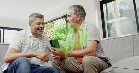 Mature friends sharing smartphone on modern couch smiling, enjoying casual home lifestyle