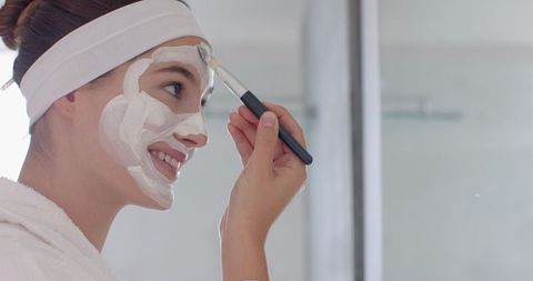 Young woman applying facial mask in bright bathroom