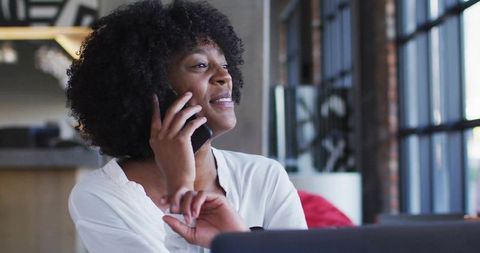 Businesswoman talking on smartphone while working at laptop in modern coworking space