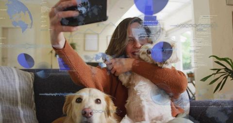Smiling woman taking selfie with two dogs on sofa while augmented reality data overlays