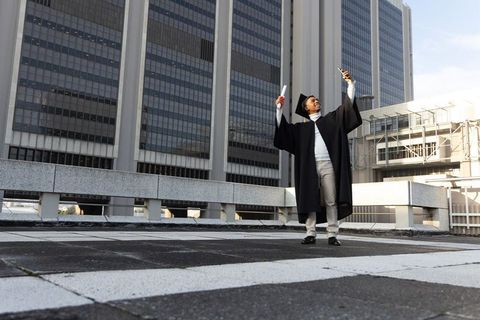 African american graduate celebrating on urban rooftop holding diploma and smartphone