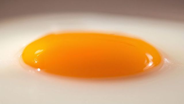 Glossy egg yolk resting on smooth white surface macro closeup with golden highlights