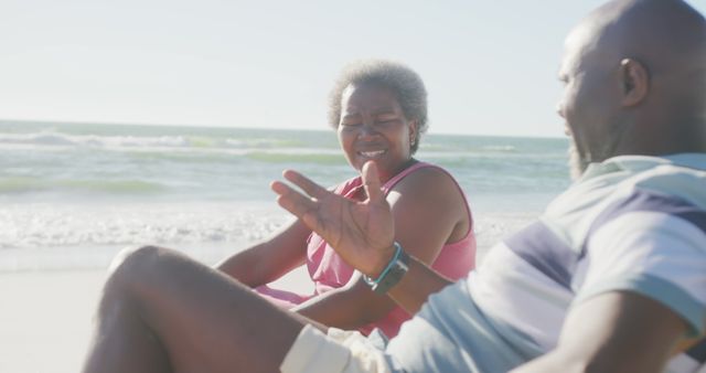 Happy senior couple sitting and talking on sandy beach. Ideal for use in advertisements related to retirement, leisure, travel, senior lifestyle, happiness, or beach vacations.