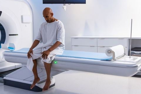 African american man waiting on ct scanner table wearing hospital gown for radiology exam
