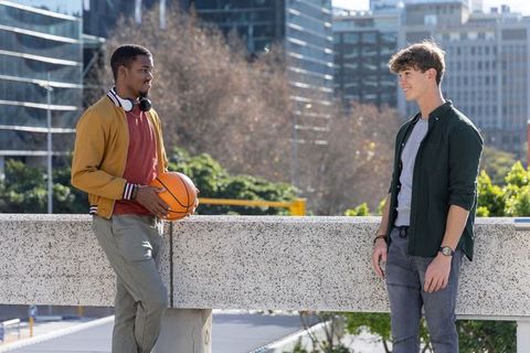 Young diverse friends chatting on urban overpass holding basketball, casual street style