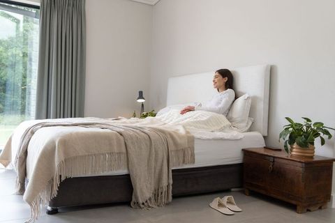 Asian woman relaxing on white bed in bright minimalist bedroom with beige throw