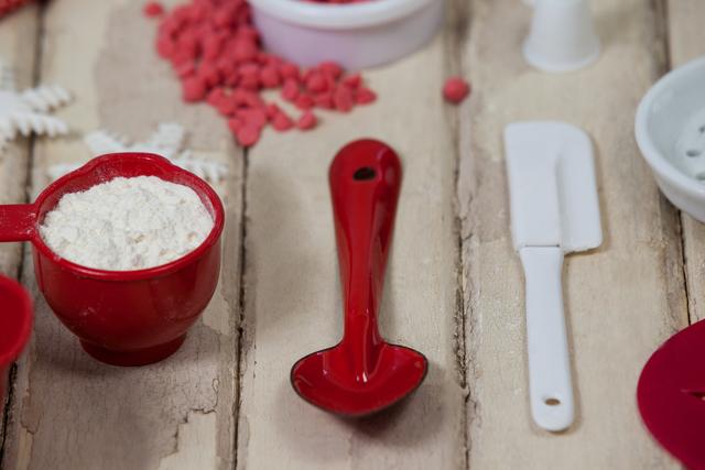 Close-up of baking tools and ingredients on a rustic wooden surface. Red measuring spoon, white spatula, and icing sugar are arranged neatly, suggesting a baking preparation scene. Ideal for use in cooking blogs, recipe websites, or kitchen-related advertisements.