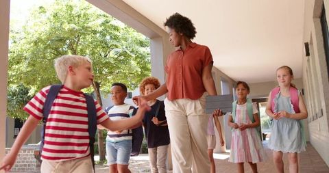 African american teacher leading diverse elementary students across sunlit school walkway