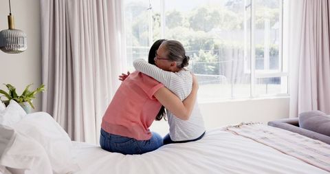 Affectionate Hug Between Senior Mother and Adult Daughter on a Cozy Bed
