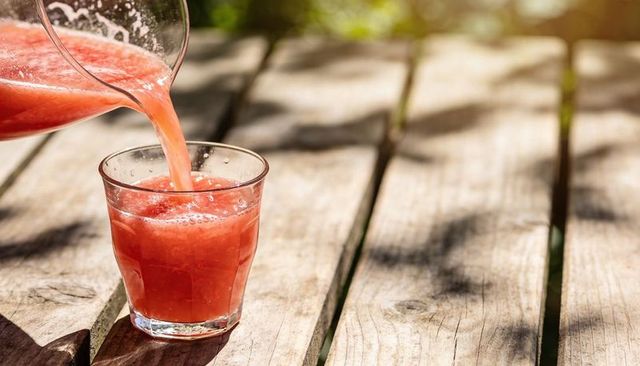 Refreshing watermelon juice pouring into glass on weathered wood table with sunlit bokeh