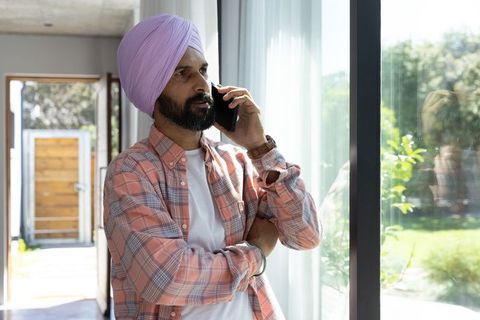 Mid adult indian man checking wristwatch while on phone by window