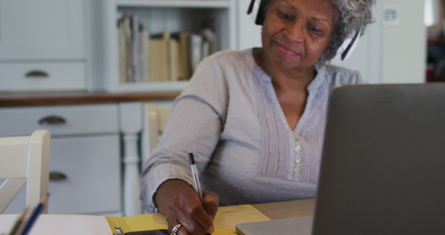 Senior woman with headphones working at home using laptop and notepad - Download Free Stock Images Pikwizard.com