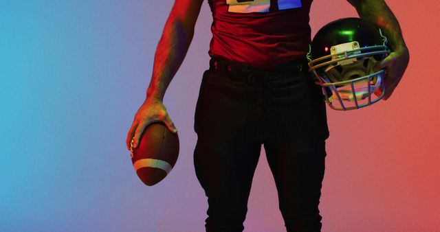 Image of midsection of caucasian american football player with ball over neon red to blue background. American football, sports and competition concept.