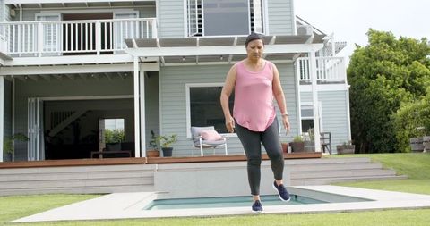 Mature woman walking along plunge pool edge in backyard wearing pink top and leggings