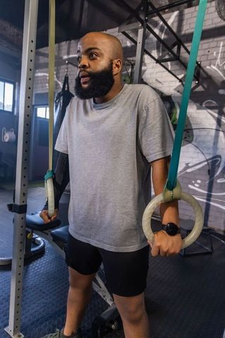 African american man training on gymnastic rings, calisthenics strength showing focus