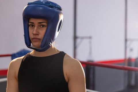 Female boxer wearing blue headguard focusing in boxing ring during training