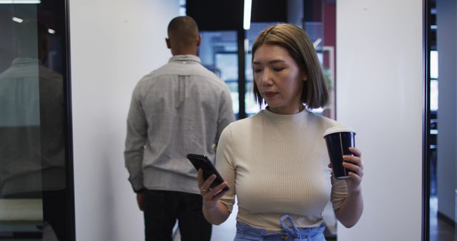 Focused Businesswoman Checking Smartphone While Holding Coffee in Office - Download Free Stock Images Pikwizard.com