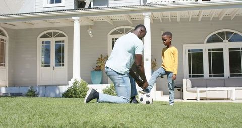 African american father tying son's soccer cleat on sunlit suburban front lawn