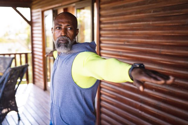 Senior African American man with a beard and bald head stretching arms while exercising in a log cabin. Ideal for use in content related to fitness, active lifestyle, retirement, solitude, and wellness. Perfect for promoting healthy living among seniors and vacation retreats.