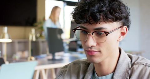 Young professional focusing on monitor in modern coworking space with tortoiseshell glasses