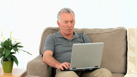 Senior Man Using Laptop on Comfortable Armchair at Home