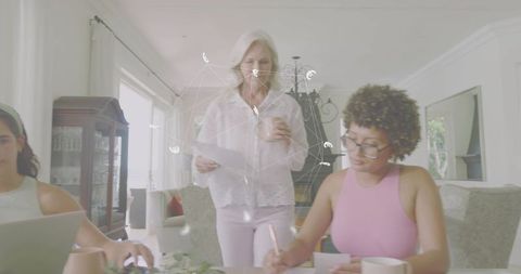 Multigenerational family collaborating at sunlit dining table, senior woman reading papers