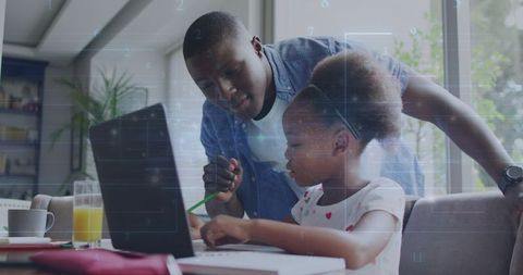 Father guiding daughter on laptop while studying at dining table