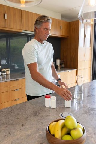 Mature man reaching for pill bottle on stone kitchen island in modern home morning routine
