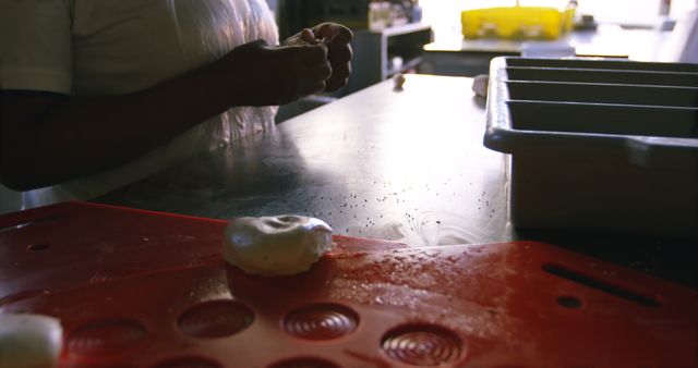 Baker is molding dough on a countertop in a kitchen, ready to make pastries. Scene includes baking tools and a dough tray nearby. This can be used to illustrate articles or blog posts on baking, recipes, or the baking profession.
