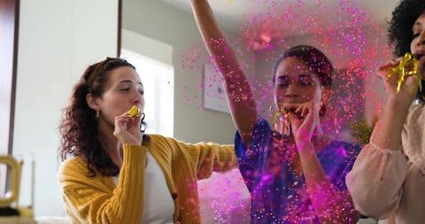 Friends celebrating with vibrant pink confetti and golden party blowers on cozy home sofa