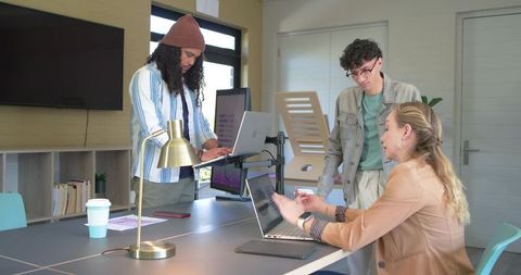 Diverse team collaborating at modern office table with laptops, standing desk and lamp