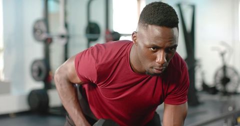 African american man performing one-arm dumbbell row in gym showing focus and strength