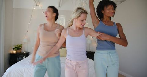 Diverse Friends Dancing on Bed in Pastel Loungewear Joyful Celebration